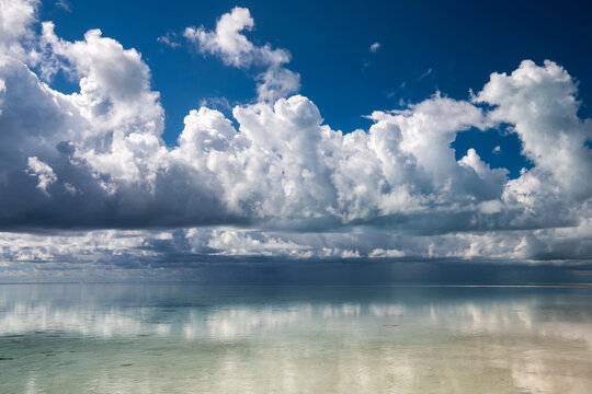 Towering cumulus clouds reflect across calm tropical water at Heron Island on the Great Barrier Reef, Queensland, Australia.
