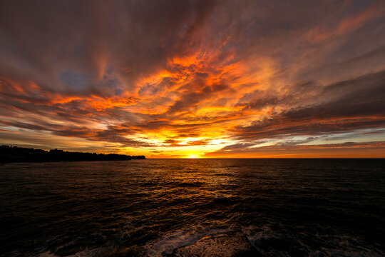 Dramatic sunrise illuminates clouds and ocean waves from a water-level perspective at Bronte Beach in Sydney, Australia.