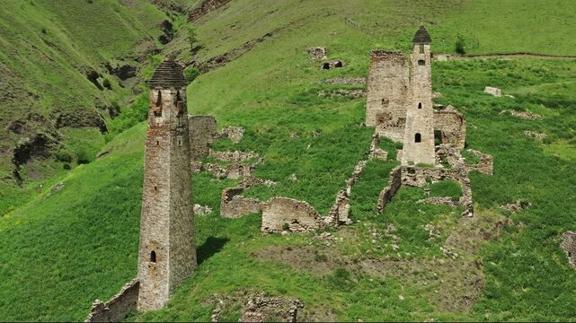 Aerial view of the historic Vovnushki stone towers situated on a lush green mountain slope in Ingushetia, Russia.