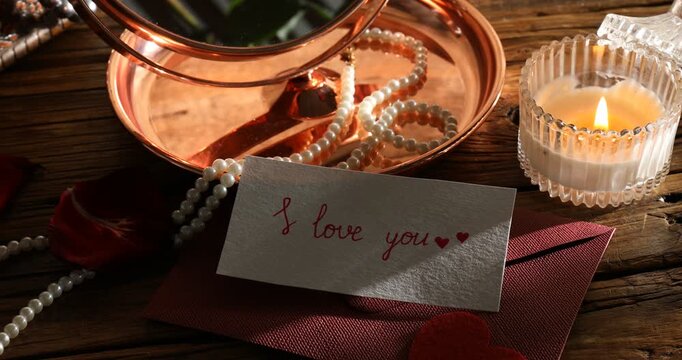 Card with phrase I Love You, envelope, burning candle, accessories and mirror on wooden table, closeup. Changing direction of light
