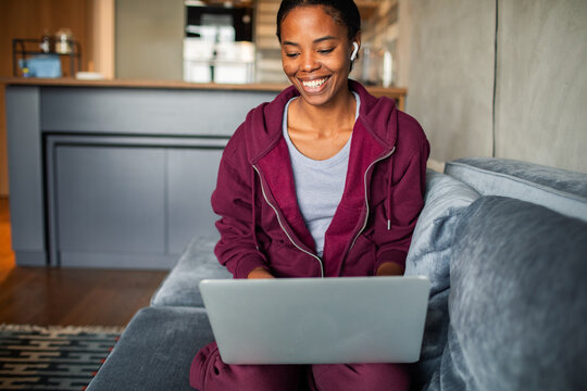 Smiling woman using laptop with earbuds at home