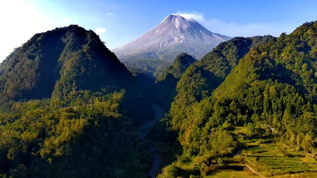 Aerial view of the majestic Mount Merapi volcano rising above the lush green hills of Nawang Jagad in Kecamatan Pakem, Daerah Istimewa Yogya, Indonesia.
