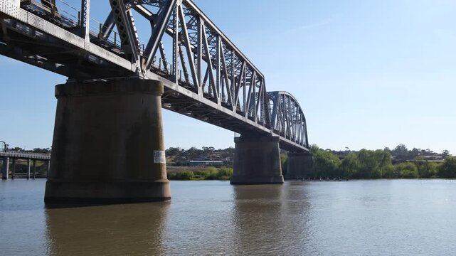 Steel truss railway bridge at Murray Bridge, South Australia, with rowers passing along the Murray River in the distance. The historic engineering structure alongside everyday river recreation.