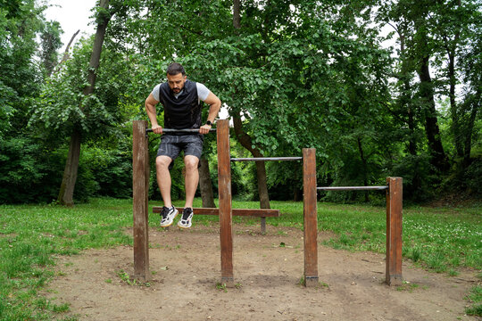 A man in athletic wear performs a dip exercise on parallel bars at an outdoor workout park