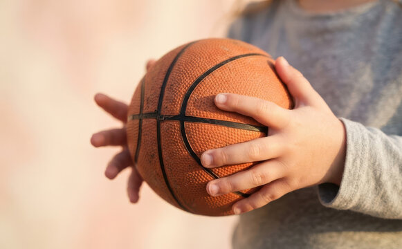 Young Child Holding Basketball Close Up in Sunset Light, Sports and Play Concept