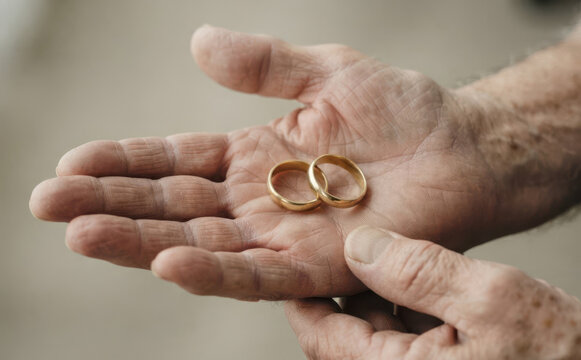 Elderly man holding two golden wedding rings in his aged palms representing everlasting love and marriage