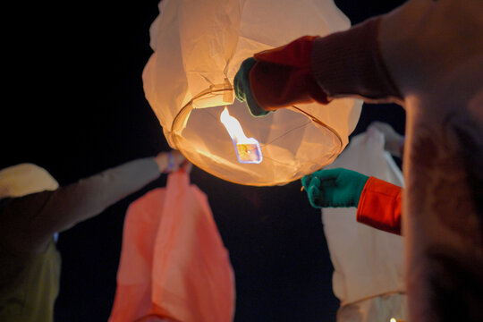 A close-up shot of a person holding a lit sky lantern against the dark night sky, preparing to release it into the air during a traditional festival or celebration.