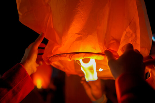 A close-up shot of a person holding a lit sky lantern against the dark night sky, preparing to release it into the air during a traditional festival or celebration.