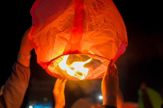 A close-up shot of a person holding a lit sky lantern against the dark night sky, preparing to release it into the air during a traditional festival or celebration.