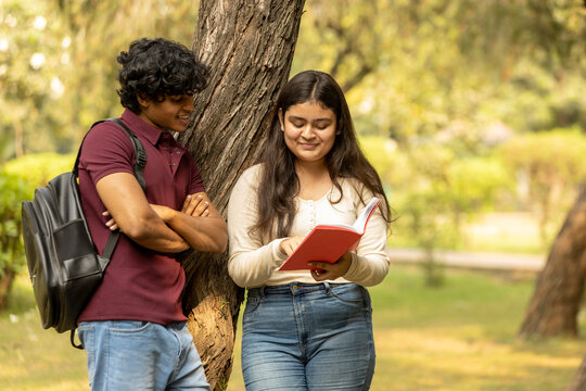 Young Indian college student couple enjoy, talking and reading notebooks while standing in the campus's park together. university lifestyle concept. Student Exams 