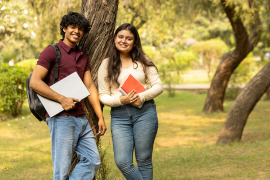 Young Indian college student couple enjoy, talking and reading notebooks while standing in the campus's park together. university lifestyle concept