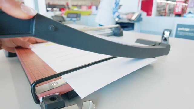 Customer service worker using a heavy duty guillotine paper cutter on a office copy center counter close up