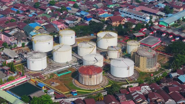 Aerial view of PT. Pertamina TBBM Samarinda oil storage facility with large white tanks surrounded by dense residential rooftops in Samarinda, East Kalimantan, Indonesia.