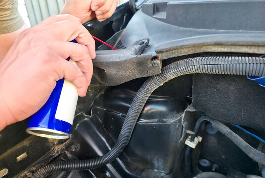 Man spraying lubricant on rubber bushings of car shock absorbers under open hood