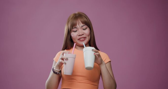 Young Asian woman with a cheerful smile holding two cups with straws on a pink background
