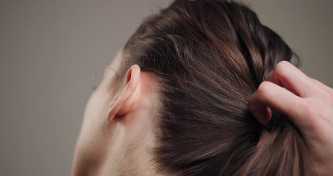 Close-up view of a young woman tying her brown hair into a ponytail