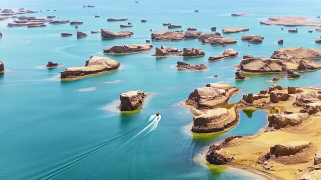 High angle shot of speed boat navigating turquoise water around unique yardang landforms in Water Yadan Geopark, Qinghai.