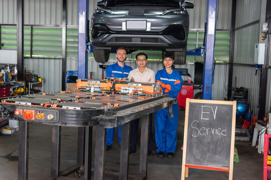 Team of electric vehicle technicians standing with an EV battery pack in an automotive workshop, representing skilled workforce, battery maintenance, engineering, teamwork