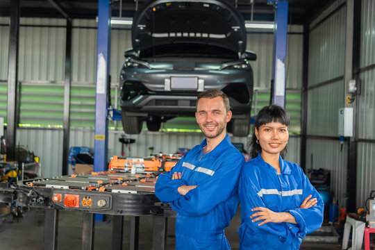 Team of electric vehicle technicians standing with an EV battery pack in an automotive workshop, representing skilled workforce, battery maintenance, engineering, teamwork