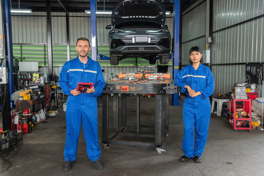 Team of electric vehicle technicians standing with an EV battery pack in an automotive workshop, representing skilled workforce, battery maintenance, engineering, teamwork