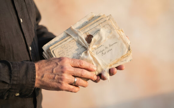 Man holding a bundle of old love letters tied with ribbon and wax seal, vintage correspondence concept