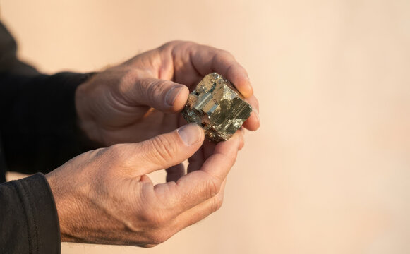 Man holding a natural pyrite cube mineral crystal in hands representing geology and mineralogy