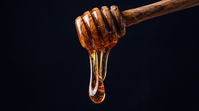Golden organic honey dripping slowly from a wooden dipper isolated on an absolute black background with copy space.