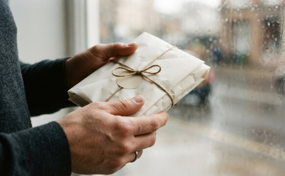 Man holding wrapped gift package parcel with twine string indoors near window