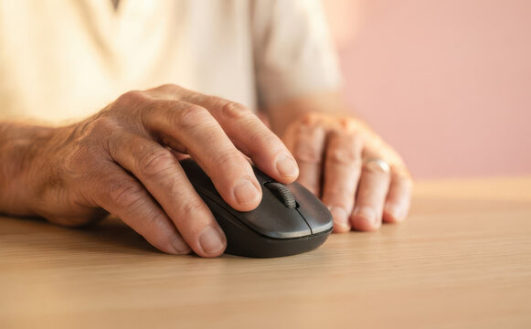 Elderly senior man using computer mouse on a desk, close up shot representing technology and aging