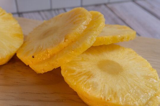 Fresh pineapple slices rest on a wooden board. Golden-yellow flesh glistens with juicy texture. Ideal for recipes, food blogs, or tropical-themed designs