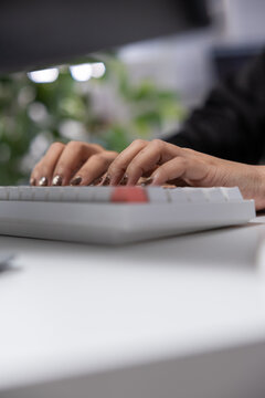 Hands typing on computer keyboard at office desk with shallow depth of field and blurred plant background Vertical