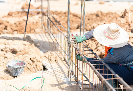 Close-up of a steel fixer assembling a rebar reinforcement cage along a trench ground structure for concrete pouring.
