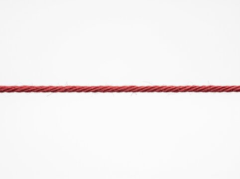 A single piece of twisted red cotton string stretched horizontally across a plain white background surface