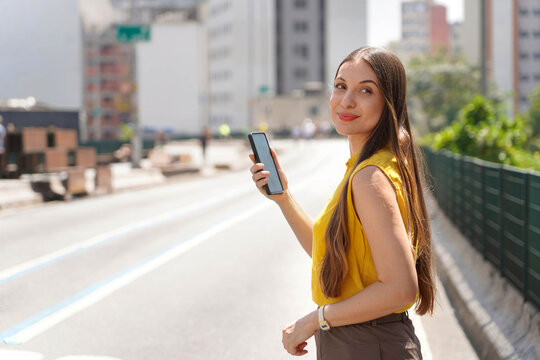 Happy smiling Brazilian woman holding smartphone on Minhocao city street in Sao Paulo, Brazil. Copy space.