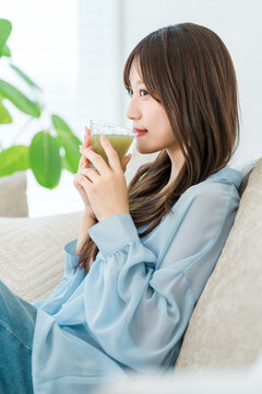グリーンスムージーを飲みながらソファでくつろぐ若い女性