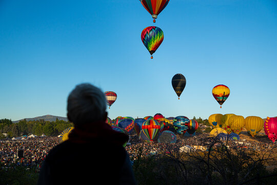 Silhouette of Spectator Watching Colorful Hot Air Balloons Rise Above a Crowded Balloon Festival