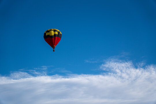 Large Red Yellow and Black Hot Air Balloon Floating Against a Soft Cloudy Blue Sky