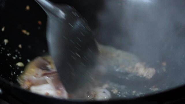 4K Chef stir-frying fresh squid rings with crushed red chilies and garlic in a hot wok, cooking process for spicy Thai stir-fried squid with holy basil concept.