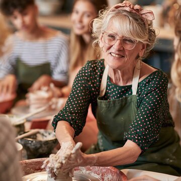 Older woman teaching pottery to young students in studio setting