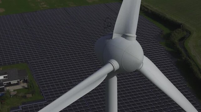 Aerial view of a large wind turbine positioned over an extensive solar panel farm in the countryside of T Zand, North Holland, Netherlands.