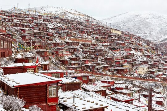 Snow-covered red buildings densely packed on a mountain slope in a high-altitude settlement
