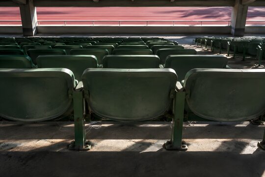 Rows of empty grandstand seats in a covered upper tier with faded green fold down shells dust and cobweb threads