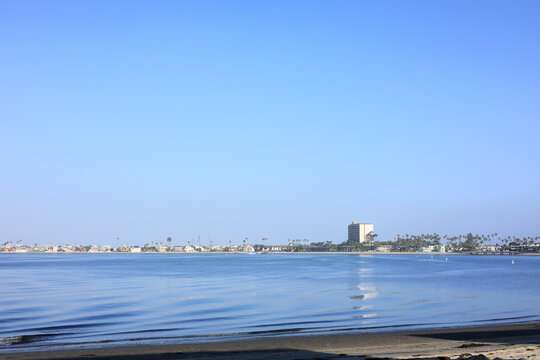 Scenic view of a distant coastal vacation rental houses and hotels over calm Mission bay water under a vast clear blue sky, San Diego, California