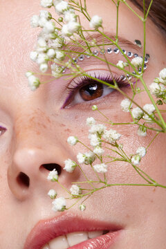 Woman looks through white Baby's Breath flowers. Female face with rhinestones and freckled skin.