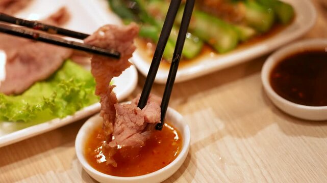 Chopsticks Dipping Sliced Pork into Spicy Sauce in Bangkok