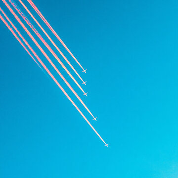 Five jet airplanes flying in formation leaving white contrails across a clear blue sky