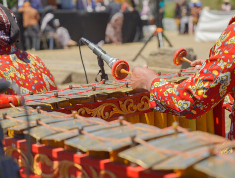 A close-up shot of a traditional Javanese gamelan musical instrument with mallets resting on it, played by musicians wearing batik shirts and blangkon during a cultural festival.