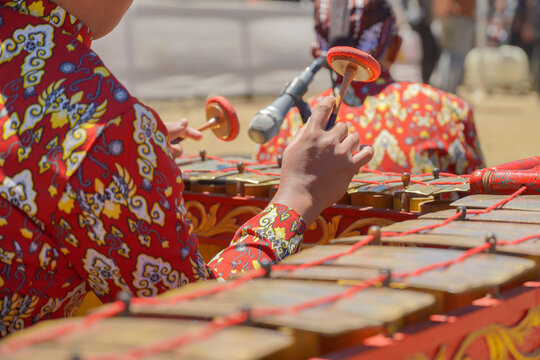 A close-up shot of a traditional Javanese gamelan musical instrument with mallets resting on it, played by musicians wearing batik shirts and blangkon during a cultural festival.