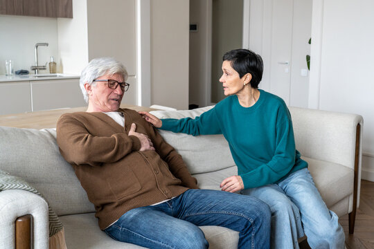 Senior man with painful cardiac attack. Elderly man struggling for breath, woman holding hand desperately, heart attack, emotional trauma, caregiving and need emergency, couple issues, aging illness