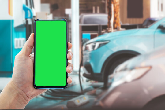 Person holding smartphone with chroma key green screen for app template mockup at EV charging station. Smart mobility and electric car concept. Human-created, not AI.